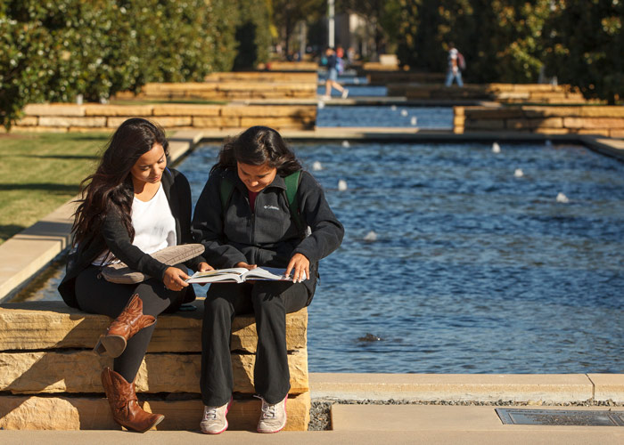 Two students sit on a limestone bench and study.